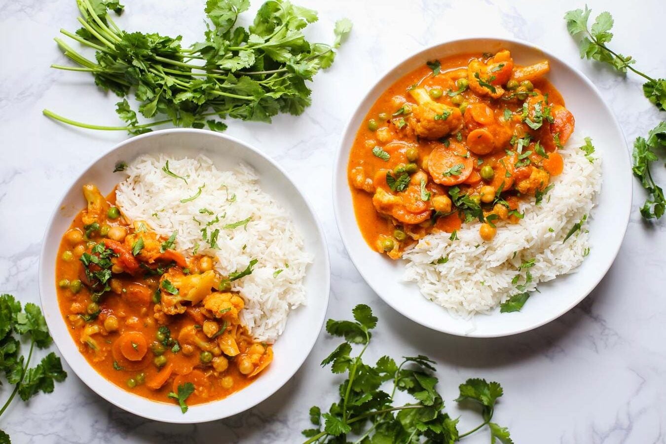 2 bowls of tikka masala and white rice on a marble background with cilantro around the bowls