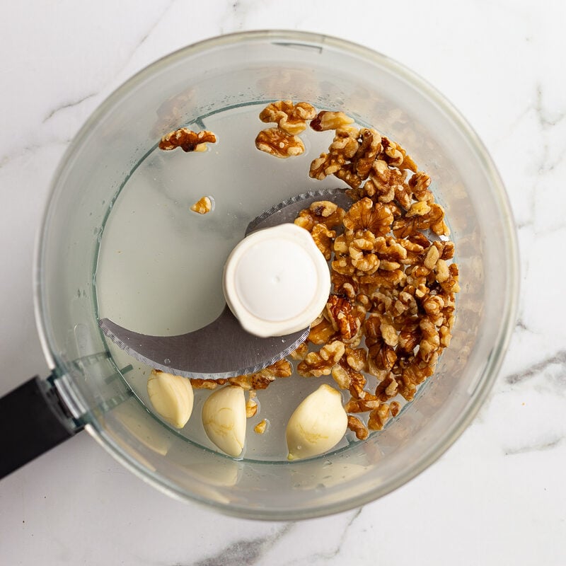Walnuts and garlic cloves in the bowl of a food processor before pulsing
