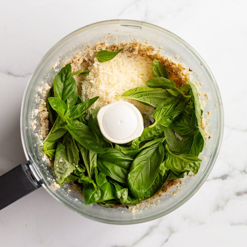 Fresh basil leaves and grated parmesan added to the food processor on top of the pulsed walnut mixture