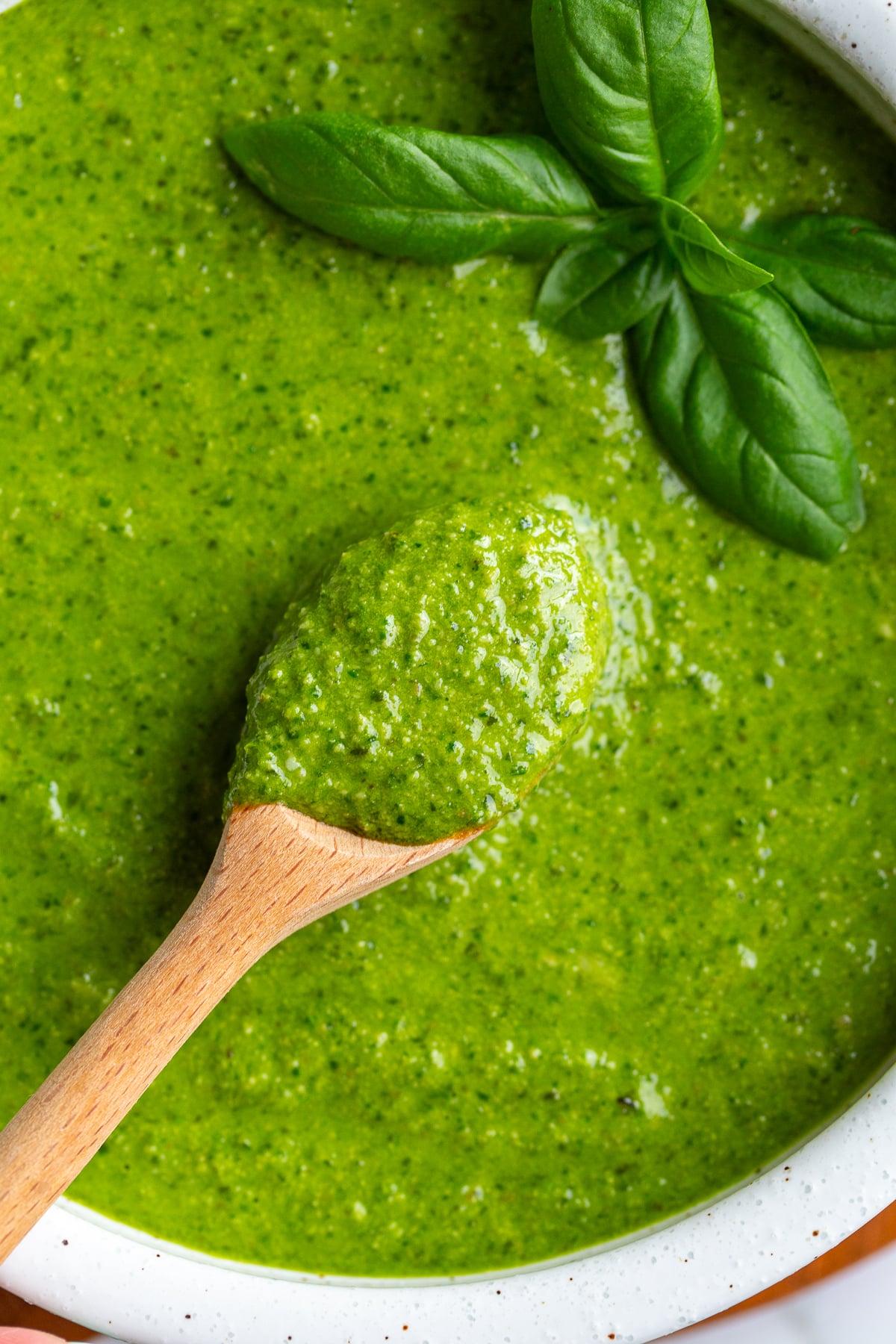 Close-up of a wooden spoon scooping thick walnut pesto from a bowl garnished with fresh basil