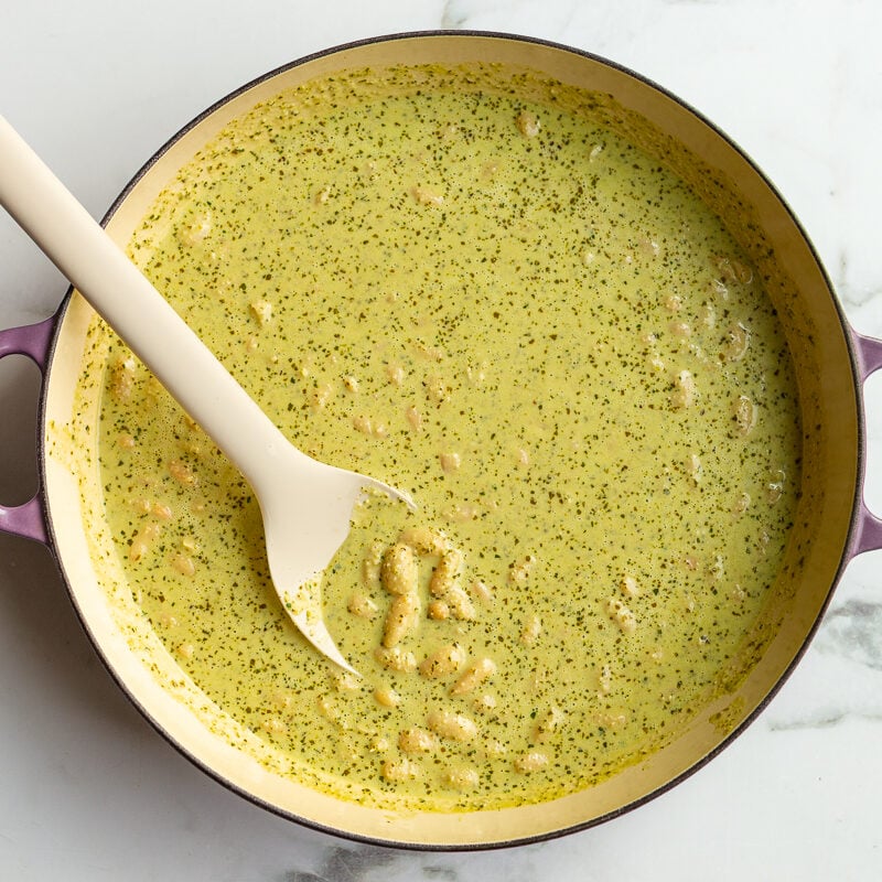 a creamy pesto sauce with beans in a large skillet