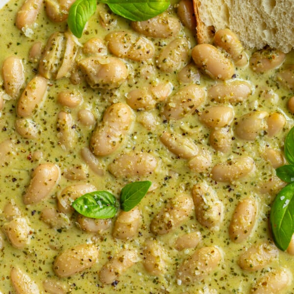 big bowl of creamy pesto beans topped with fresh basil and fresh bread hanging out the side