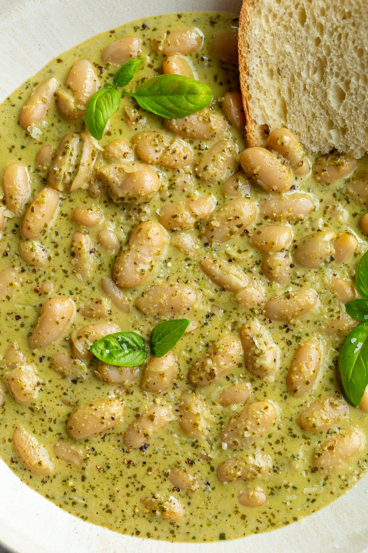 big bowl of creamy pesto beans topped with fresh basil and fresh bread hanging out the side
