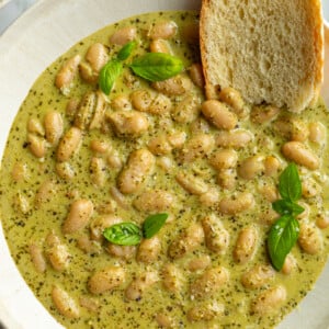 big bowl of creamy pesto beans topped with fresh basil and fresh bread hanging out the side