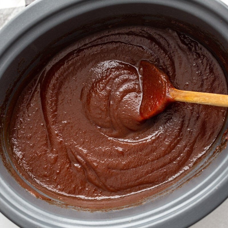 blended and smooth apple butter in a crockpot with a wooden spoon on the side