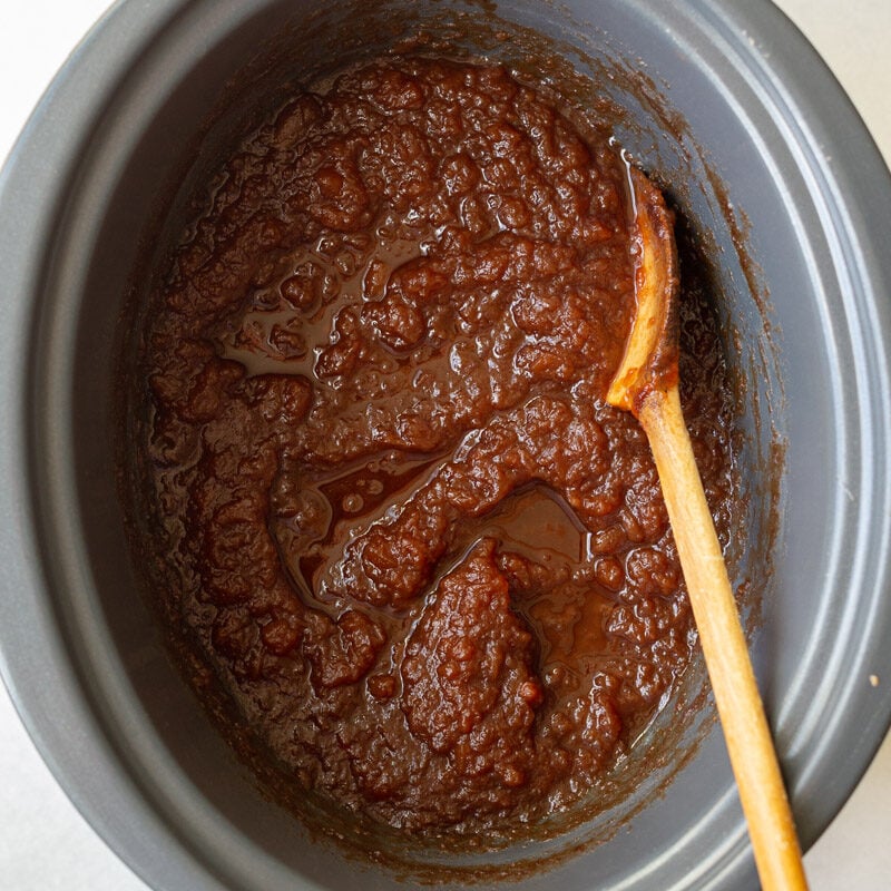 unblended apple butter in a crockpot with a wooden spoon on the side