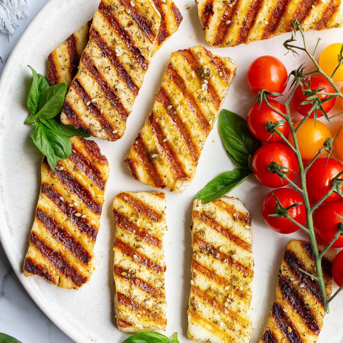 Grilled halloumi slices with golden grill marks arranged on a plate with fresh basil leaves and cherry tomatoes