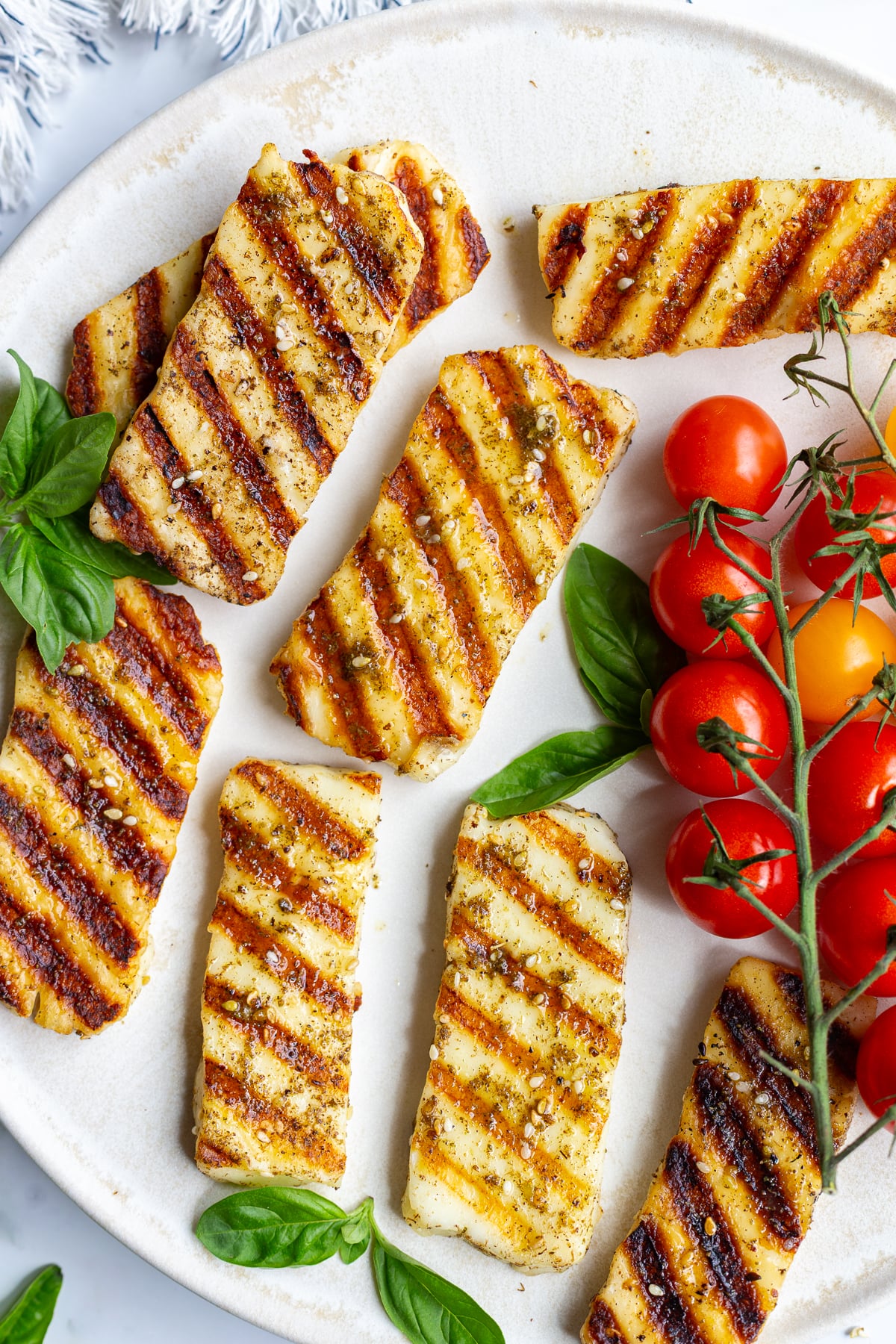 Close-up of grilled halloumi slices with visible char marks, garnished with basil and cherry tomatoes