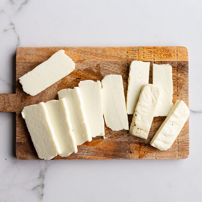 Halloumi cheese sliced into thick planks on a wooden cutting board