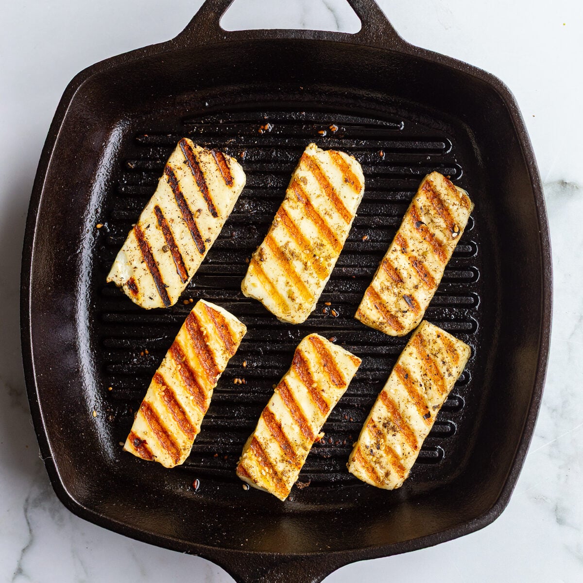 Marinated halloumi slices on a cast iron grill pan with golden grill marks