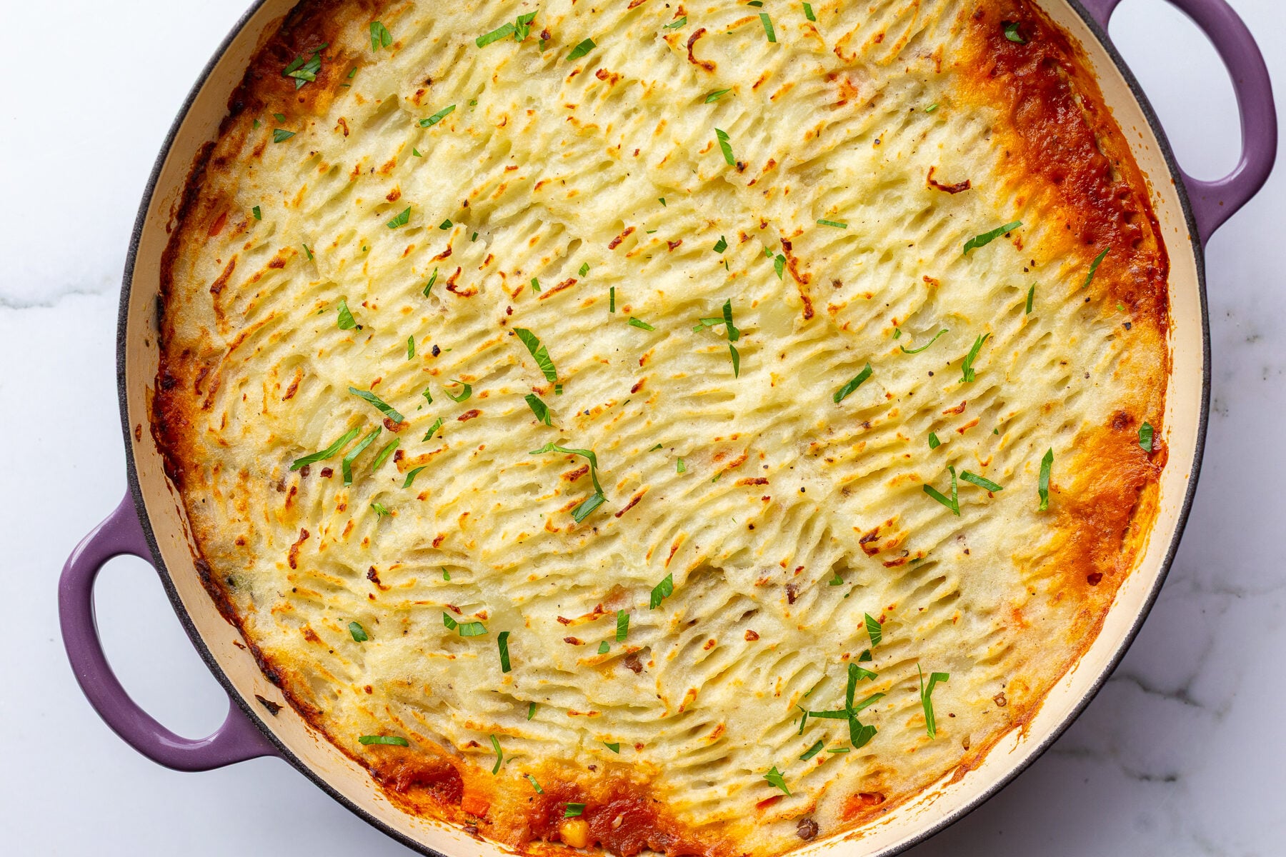 vegan shepherd's pie with crispy potato topping and red liquid that's bubbled out around the edges. The pie is in a large purple skillet