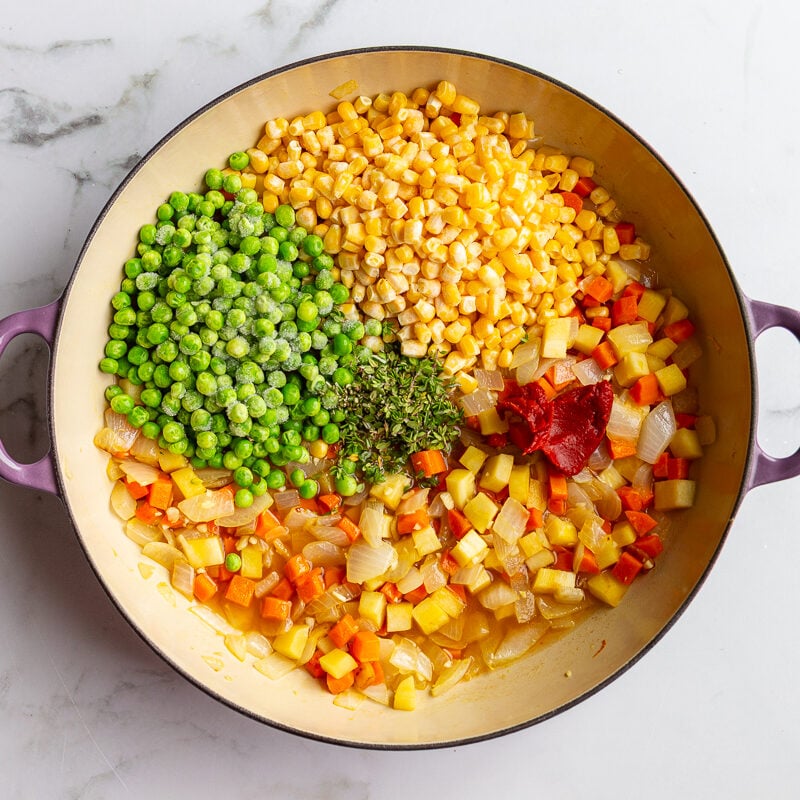 step 2 in making vegetarian shepherds pie: onion, parsnips, and carrots sauteed in a large skillet with frozen corn and peas on top before being stirred in