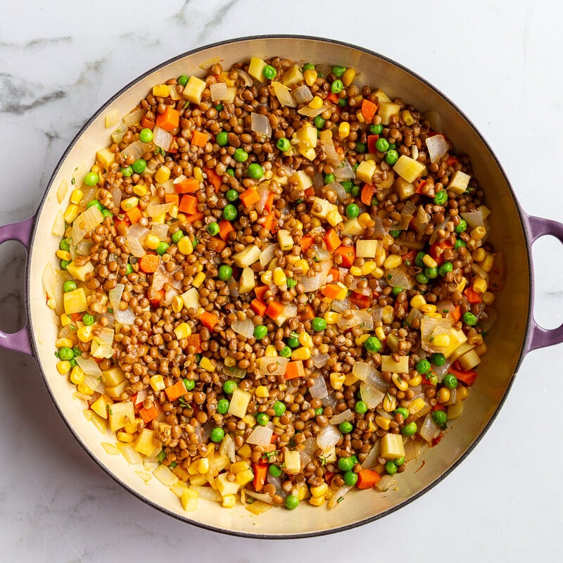 step 3 in making vegetarian shepherds pie: onion, parsnips, and carrots sauteed in a large skillet with corn, peas and lentils