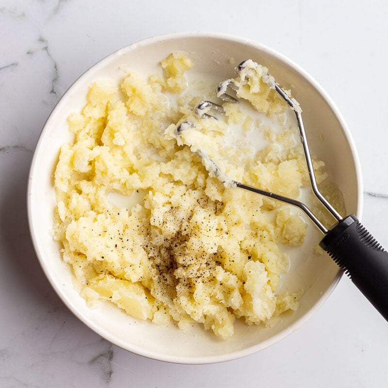 step 5 in making vegetarian shepherds pie: mashed potatoes being mashed in a large white bowl