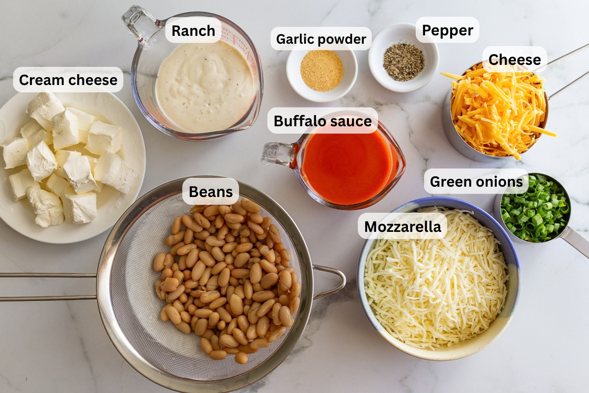 labeled ingredients needed for vegetarian buffalo chicken dip including beans, ranch, buffalo sauce, pepper, cheese, and green onions