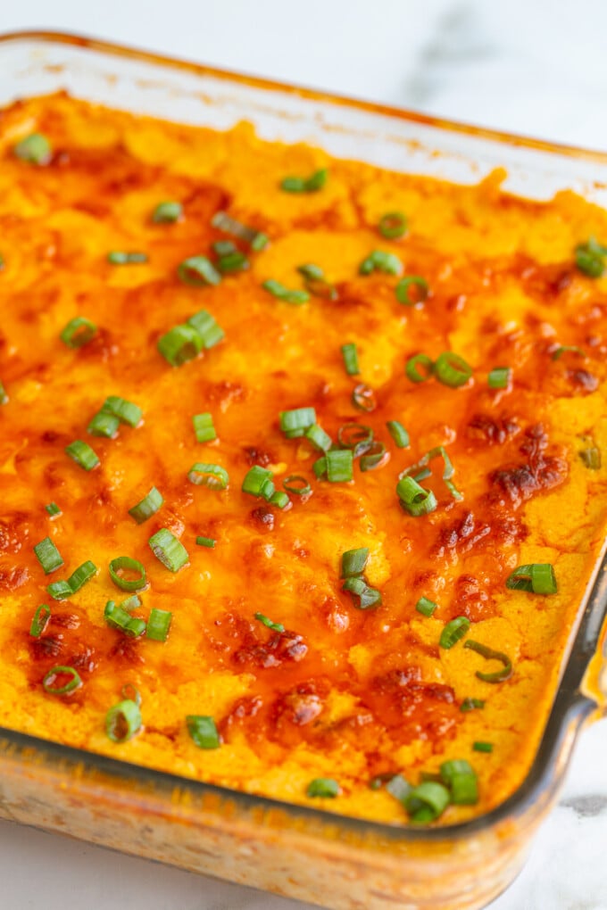 vegetarian buffalo dip in a glass baking dish with a golden cheesy topping