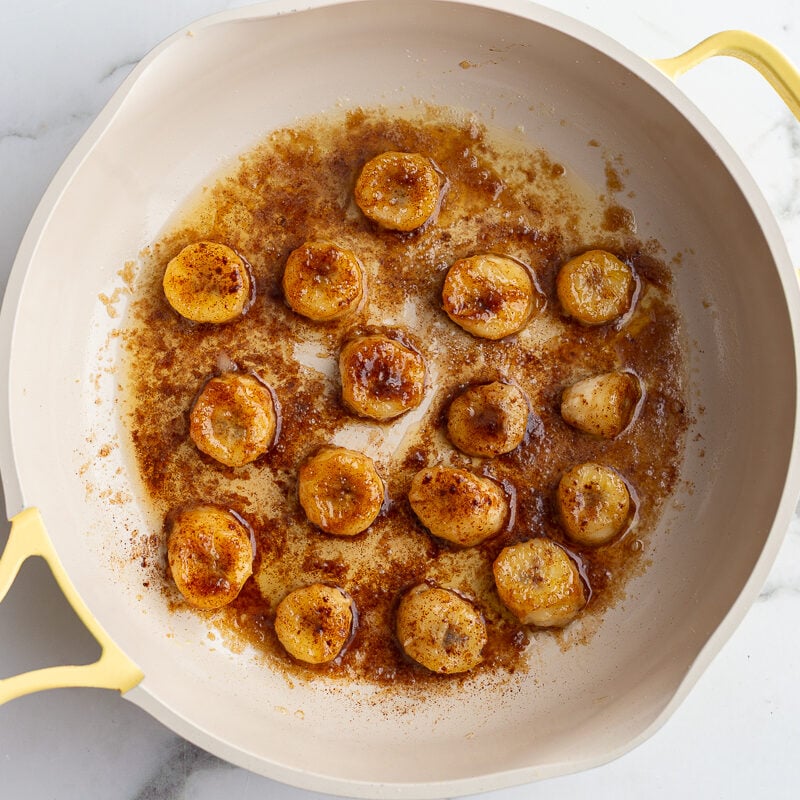 bananas and brown sugar cooking in a yellow skillet to caramelize them