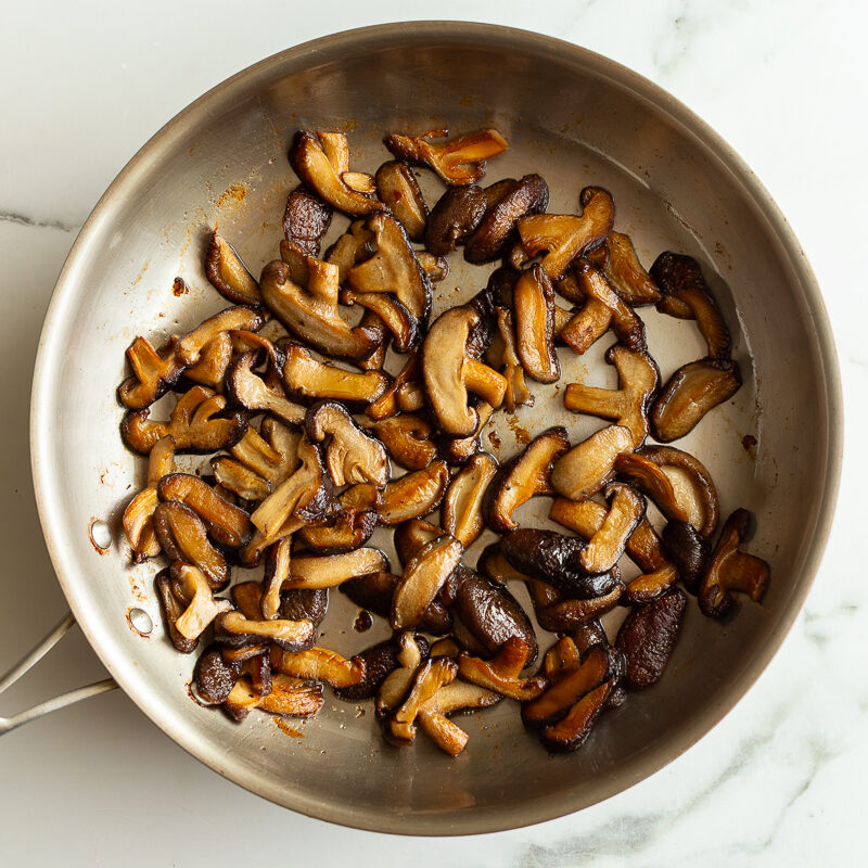 thinly sliced shiitake mushrooms sauteeing in a skillet