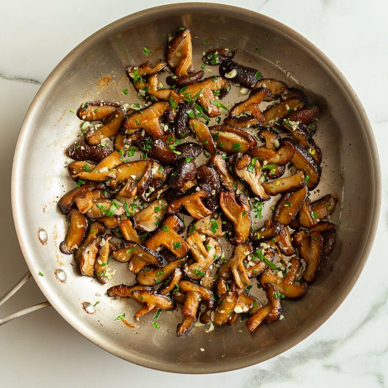thinly sliced shiitake mushrooms sauteeing in a skillet with garlic and herbs