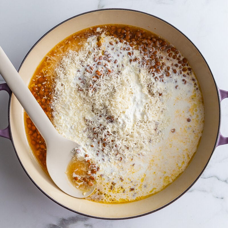 ingredients in a large skillet to make marry me lentils where you can see the lentils, cream, broth, and Parmesan cheese
