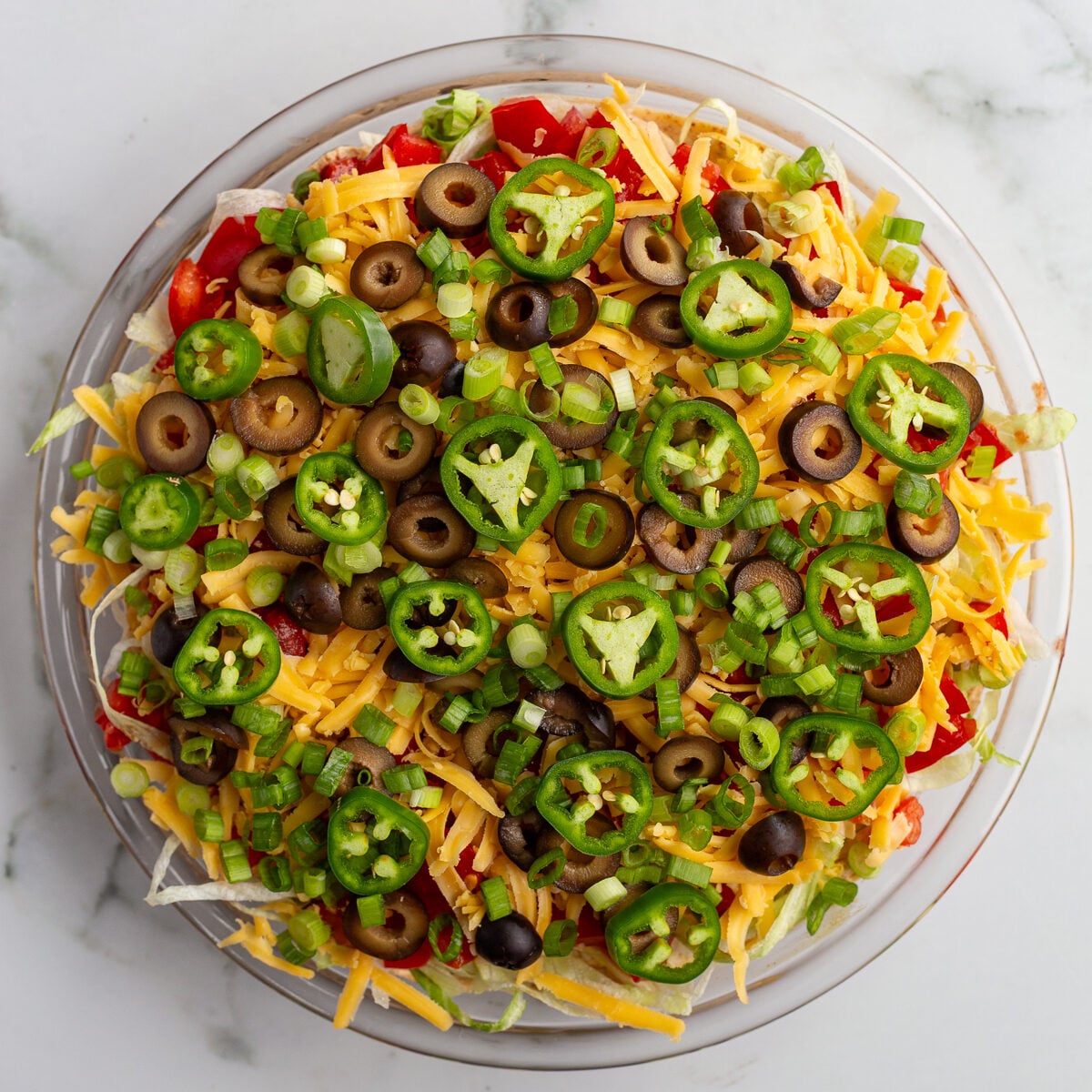 taco dip with cream cheese that's layered liek a 7 layer dip with beans, cream cheese, lettuce, cheese, jalapeno, olives, and tomato