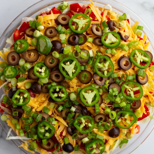 taco dip with cream cheese that's layered liek a 7 layer dip with beans, cream cheese, lettuce, cheese, jalapeno, olives, and tomato
