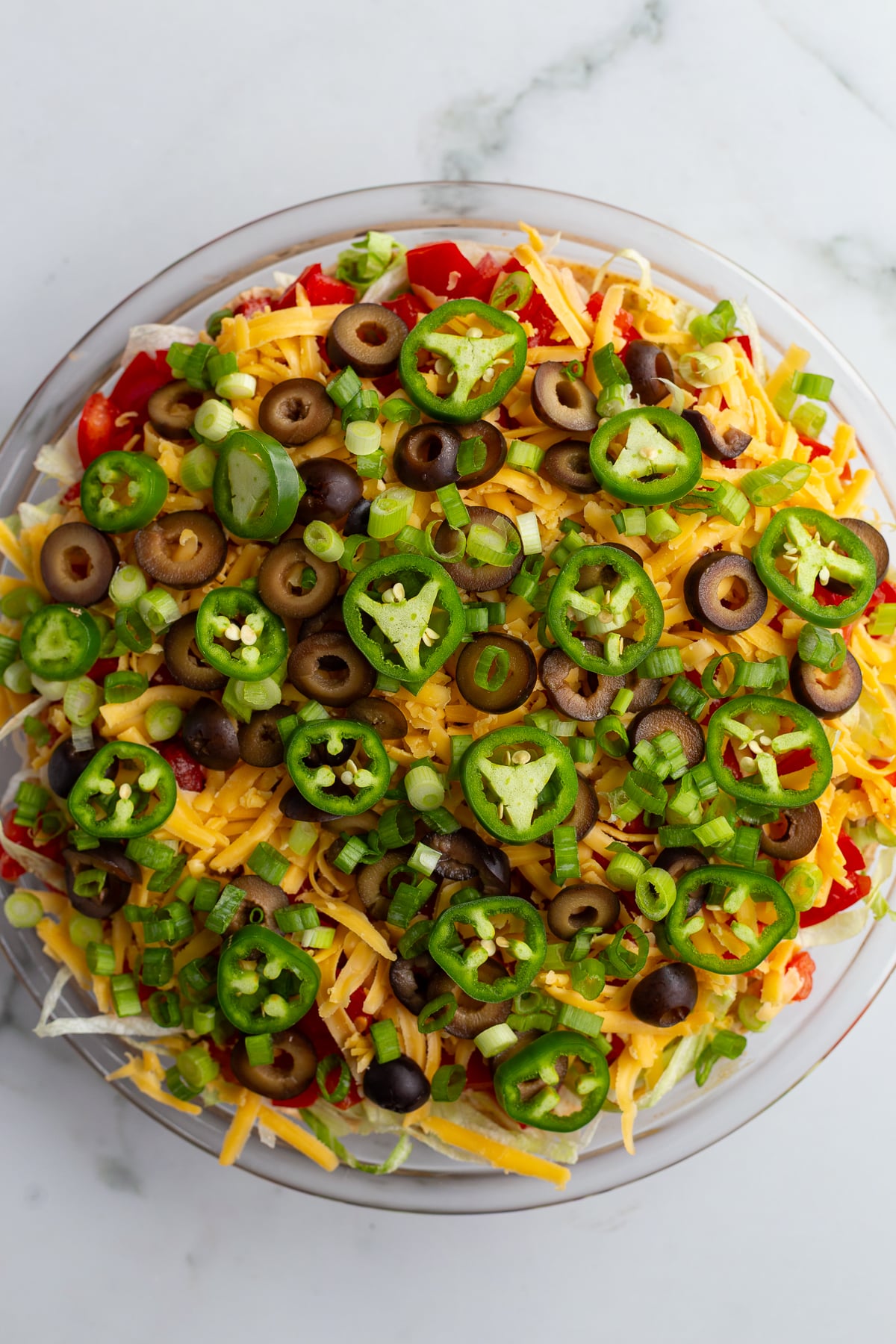 taco dip with cream cheese that's layered liek a 7 layer dip with beans, cream cheese, lettuce, cheese, jalapeno, olives, and tomato