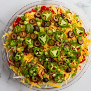 taco dip with cream cheese that's layered liek a 7 layer dip with beans, cream cheese, lettuce, cheese, jalapeno, olives, and tomato