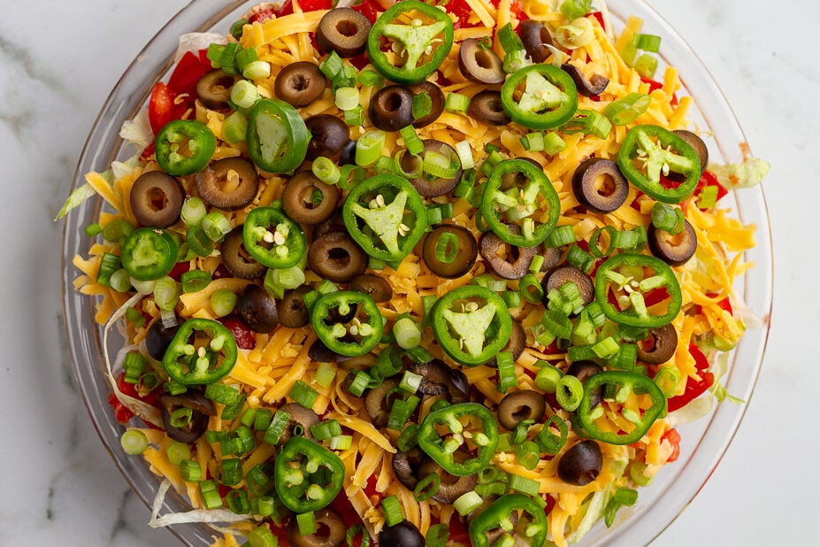 taco dip with cream cheese that's layered liek a 7 layer dip with beans, cream cheese, lettuce, cheese, jalapeno, olives, and tomato