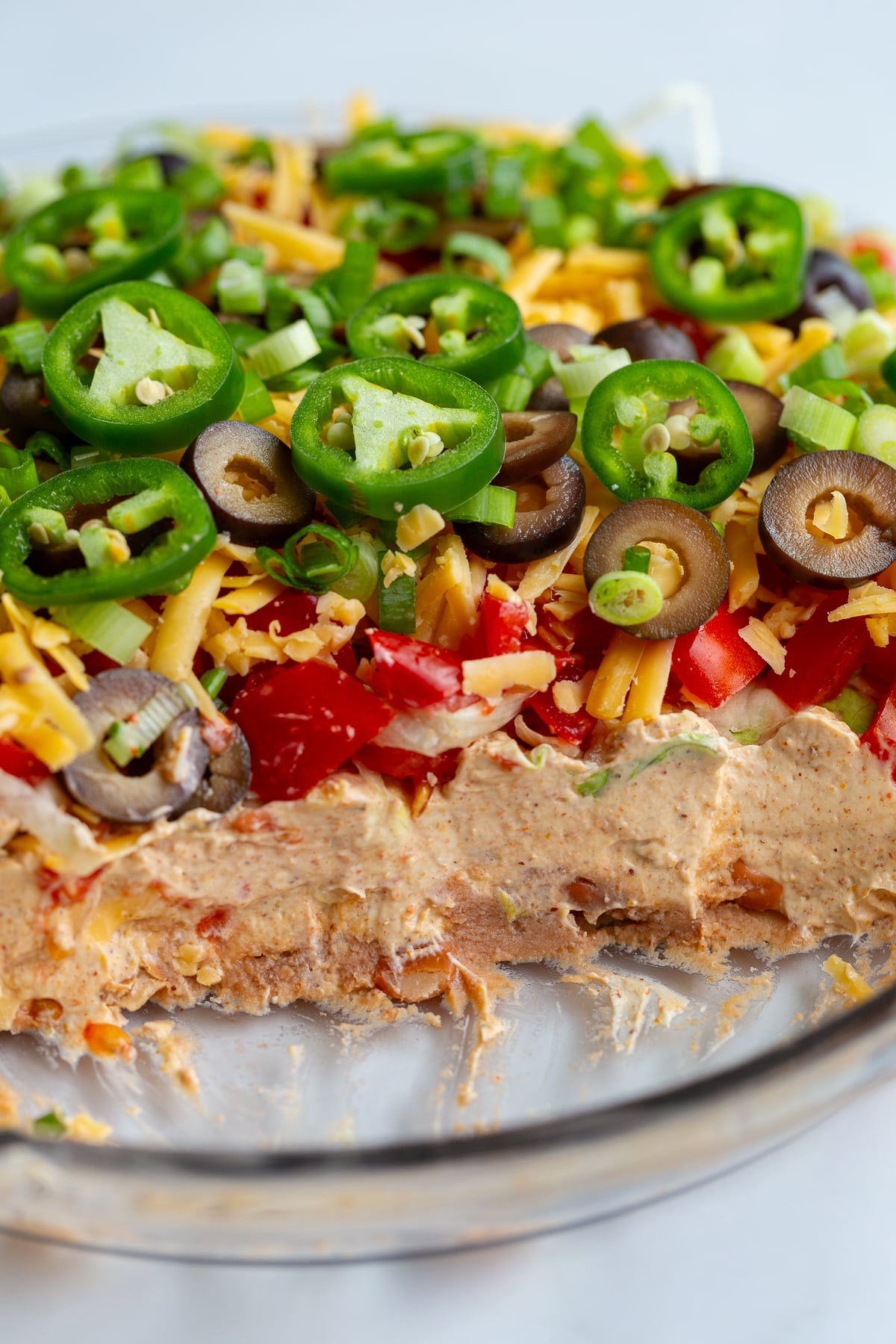 taco dip with cream cheese that's layered like a 7 layer dip with beans, cream cheese, lettuce, cheese, jalapeno, olives, and tomato. scoops are taken out so you can see the inside of the dip