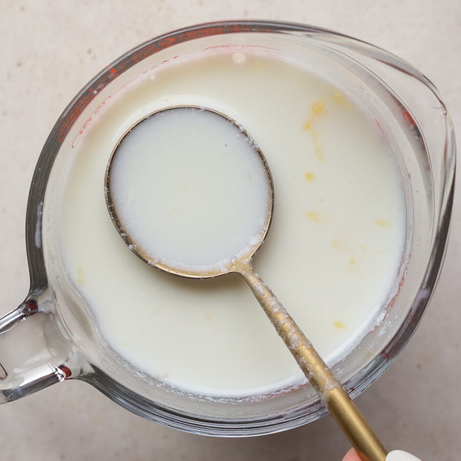 Using a spoon to stir milk and lemon juice in a spouted measuring glass.