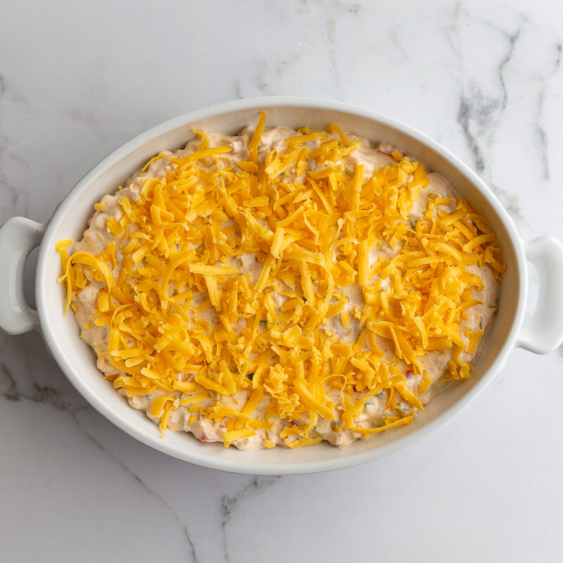 cream cheese corn dip in an oval dish topped with unmelted cheese