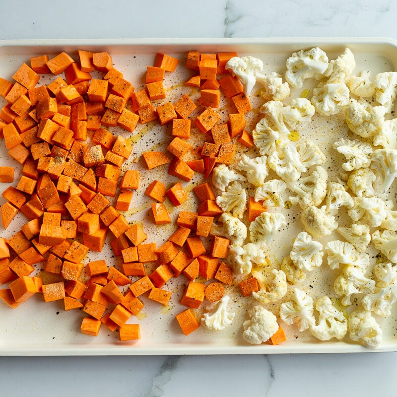 sweet potato and cauliflower florets on a baking sheet before being roasted
